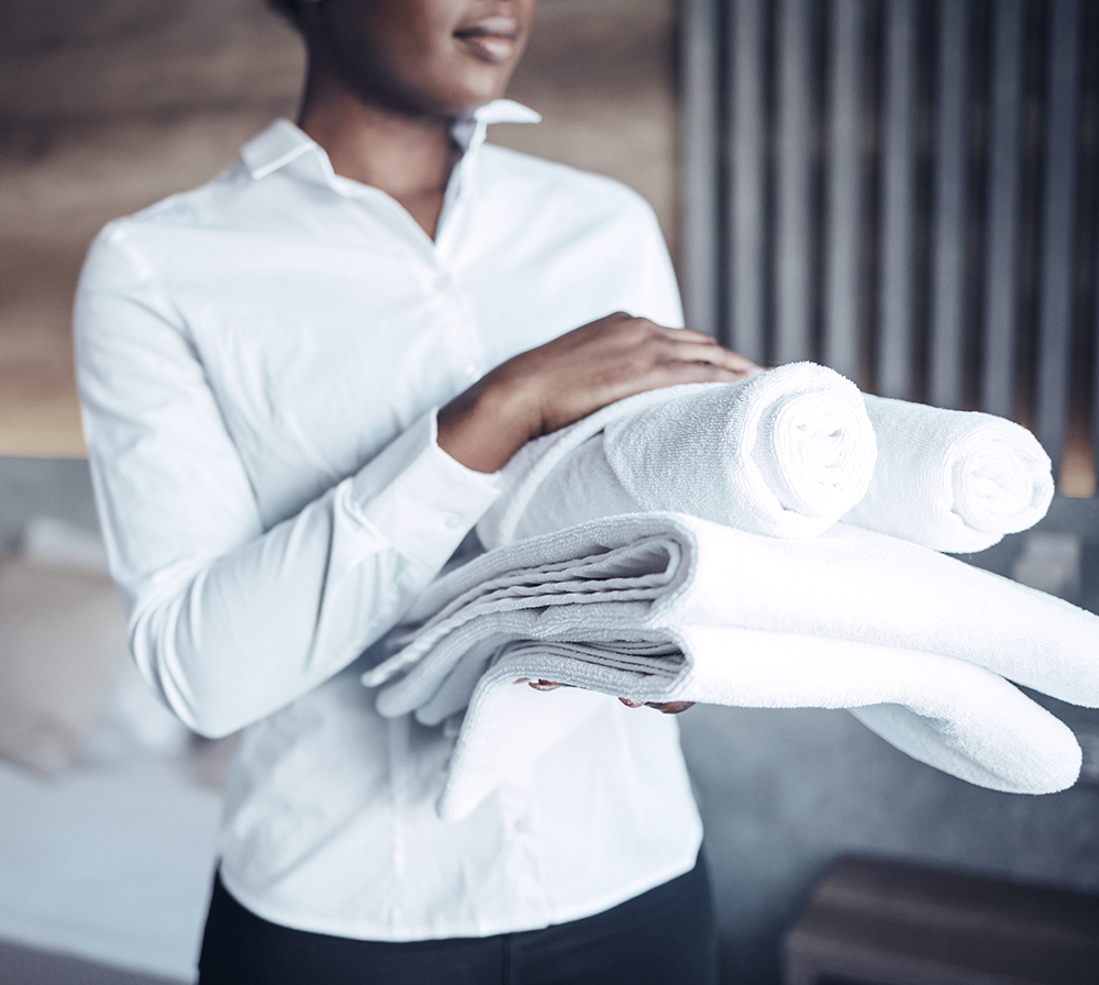 A woman in a white shirt is holding a stack of towels.