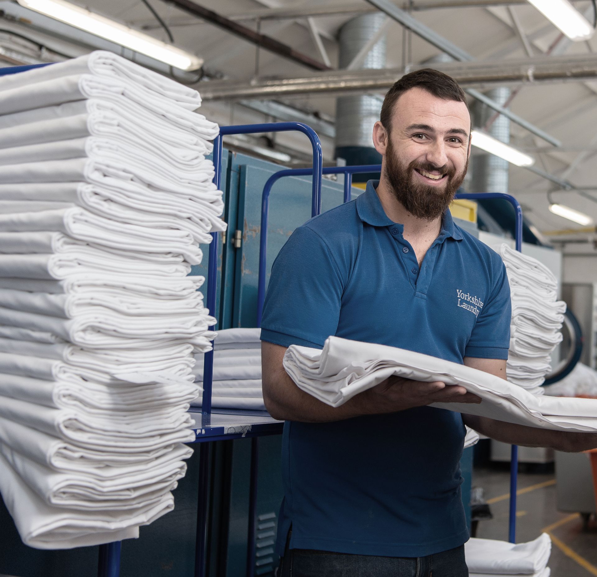 A man in a blue shirt is holding a stack of white towels