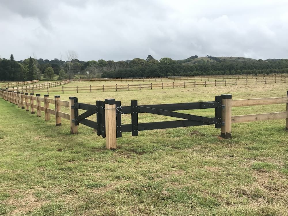 A Wooden Fence Surrounds a Grassy Field with Trees in The Background — Adam's Sawmill in Bonville, NSW