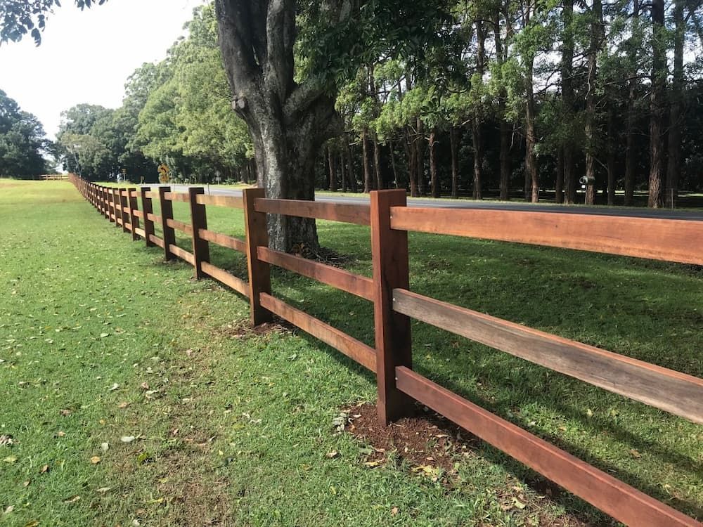 A Wooden Fence Surrounds a Grassy Field with Trees in The Background — Adam's Sawmill in Bonville, NSW