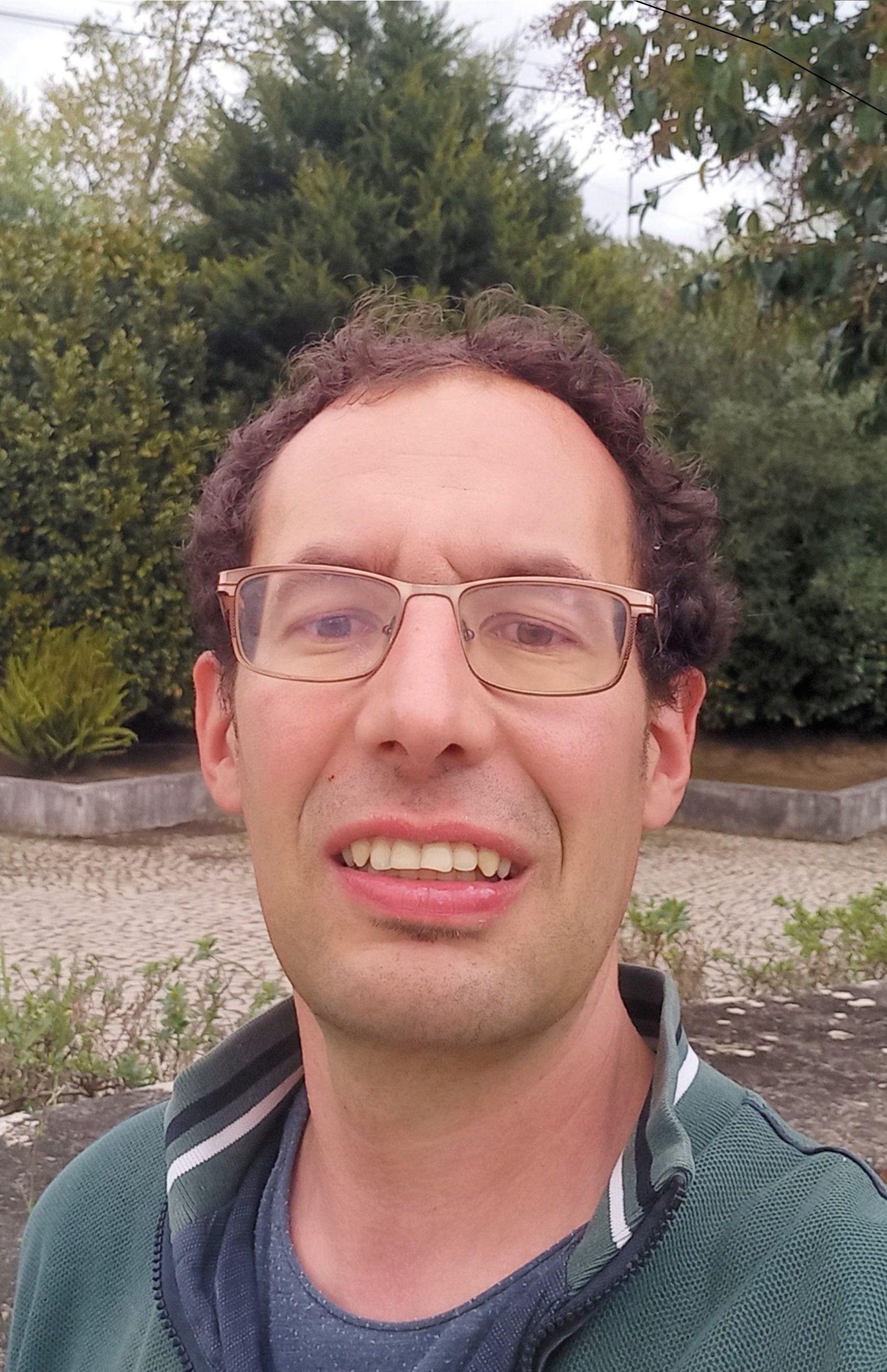 A man wearing glasses and a green jacket is smiling for the camera.