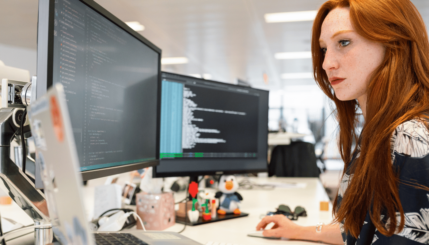 A woman is sitting at a desk looking at a computer screen.