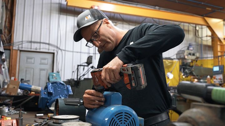 Un homme travaille sur un moteur avec une perceuse dans un garage.