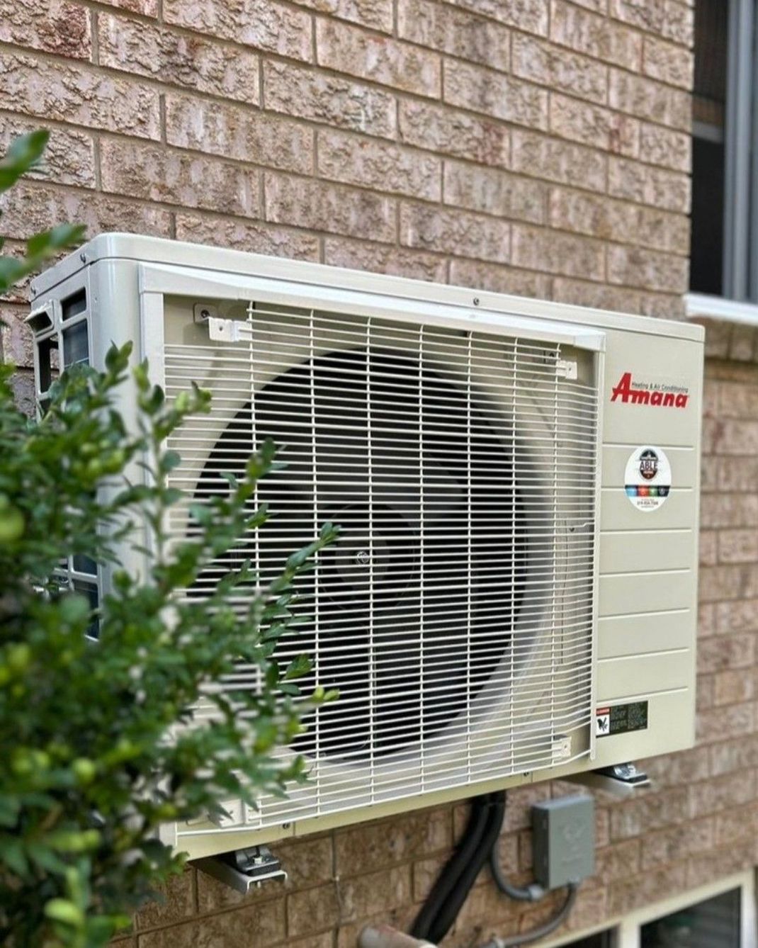 A white air conditioner is mounted on the side of a brick building.