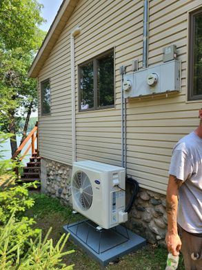 A man is standing next to a large air conditioner on the side of a house.