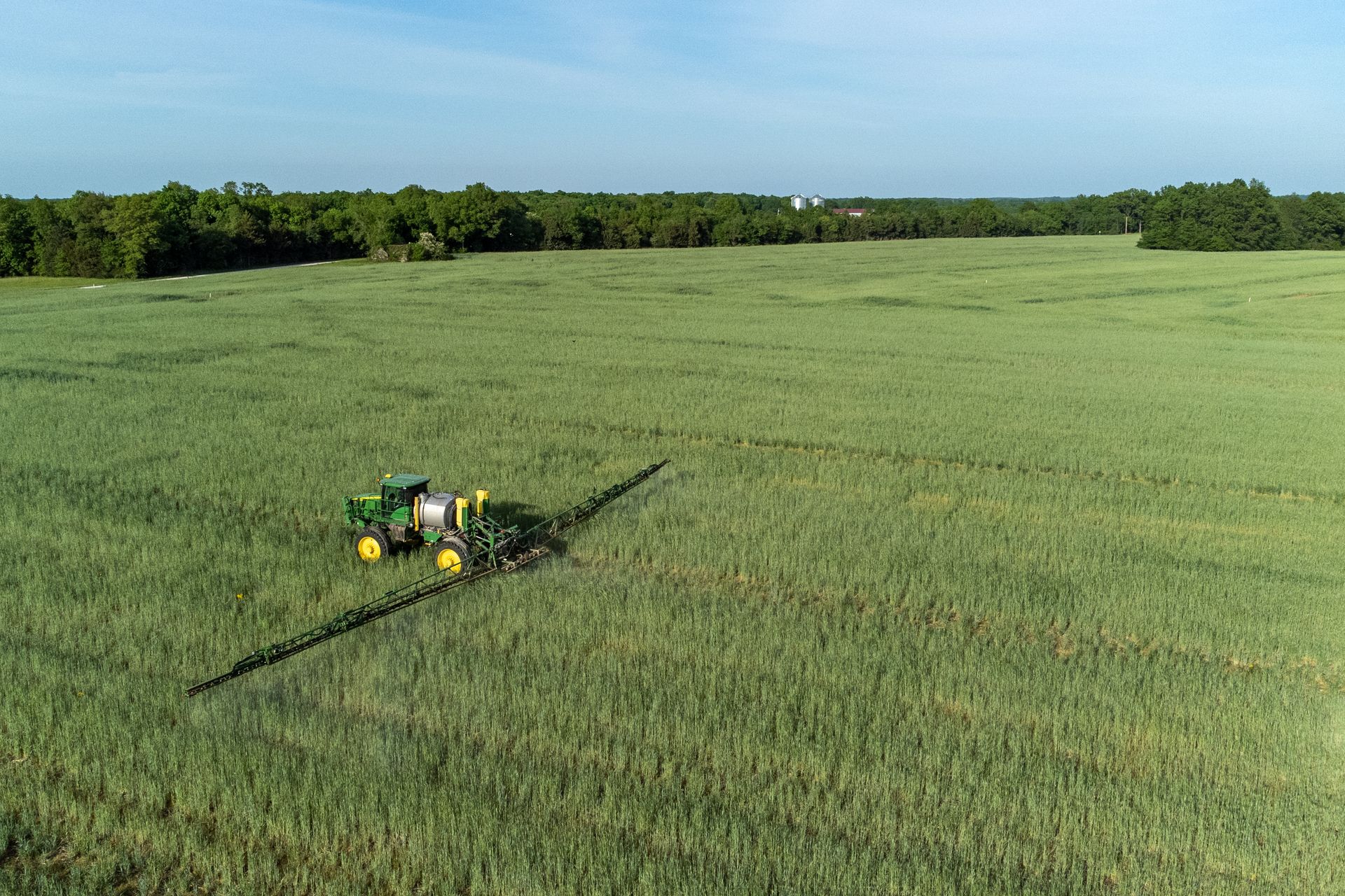 An aerial view of a tractor spraying a field of wheat.