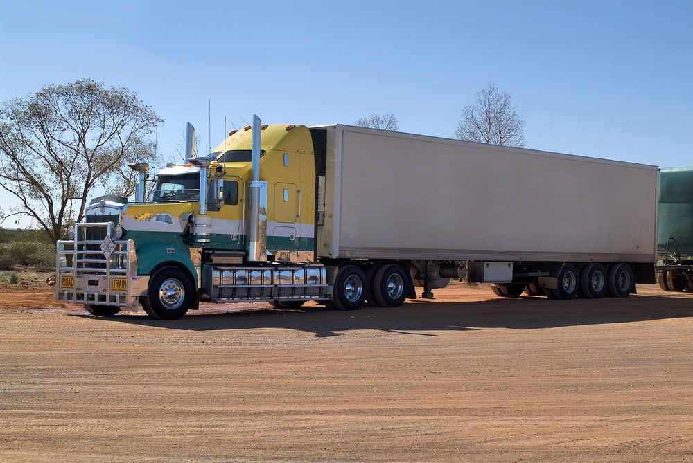 A Yellow And Green Semi Truck Is Parked On A Dirt Road  — Castledine's Truck Painting & Repairs in Fountaindale, NSW