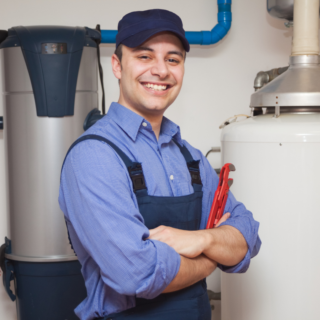 Smiling male technician in uniform, arms crossed, near plumbing and equipment.