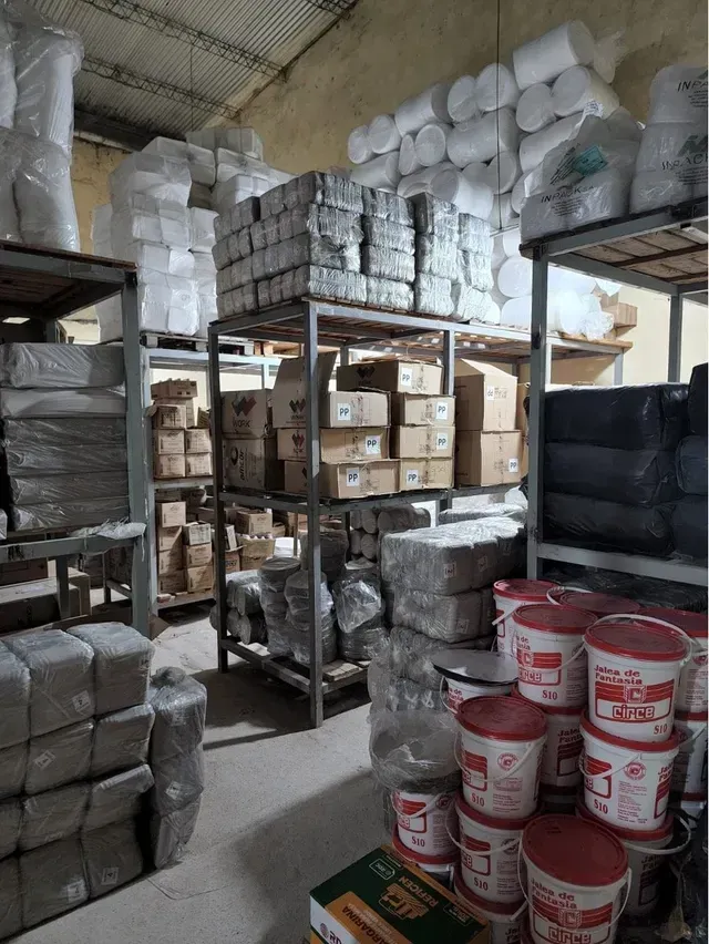 Trastero con estanterías metálicas repletas de cajas, artículos envueltos y cubos de pintura rojos y blancos.