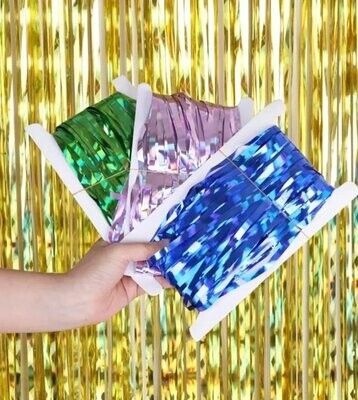 Borlas metálicas en magenta, plata, rojo, azul, verde y dorado, con una mano sosteniendo cintas azules en un círculo insertado.