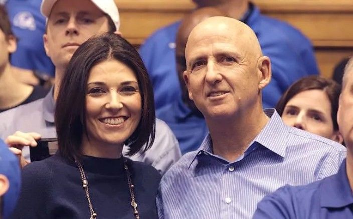 Woman and bald man smiling, possibly at a sporting event, wearing blue.