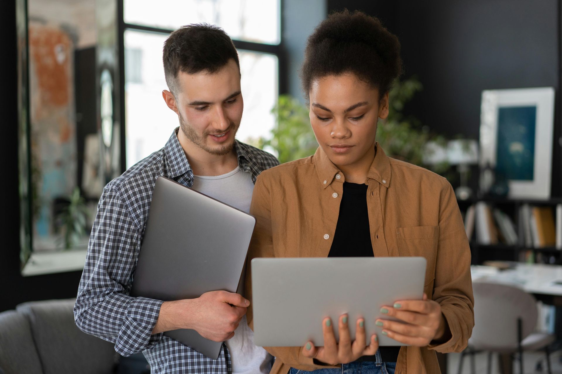 Man and woman looking at laptop screen in a modern room; man holds a laptop.