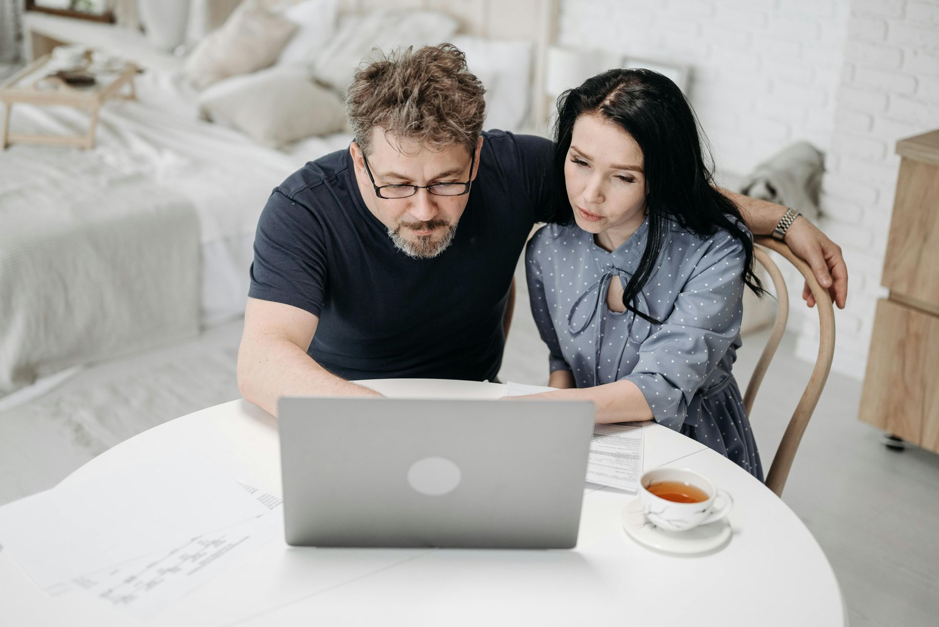 Couple looking at a laptop together at a table, tea nearby.