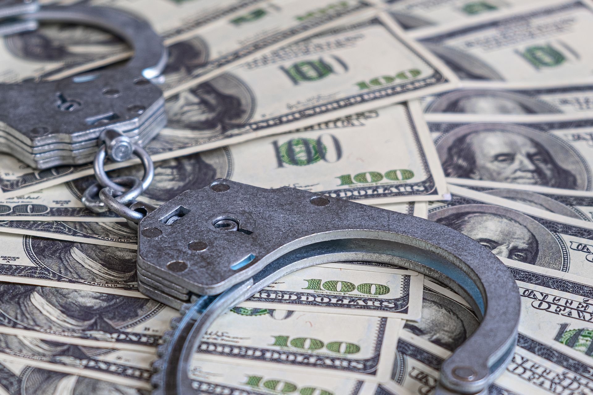 Handcuffs resting on a pile of one hundred dollar bills, suggesting crime.