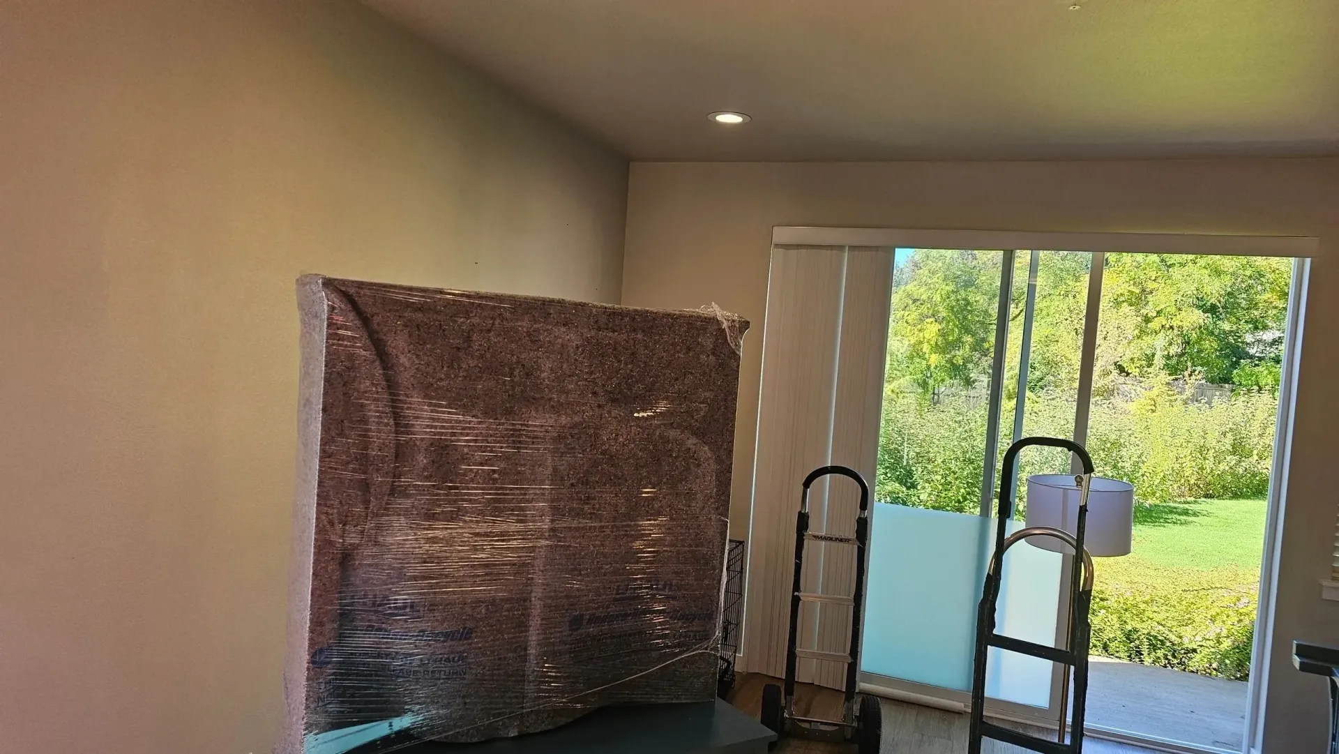A large piece of furniture is wrapped in plastic in a living room.