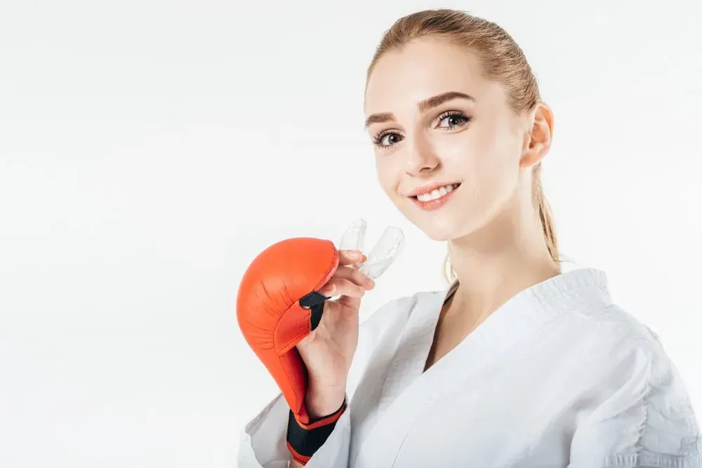 A Woman in a Karate Uniform is Wearing Boxing Gloves and Holding a Mouth Guard — Twin Towns Denture Clinic In Laurieton, NSW