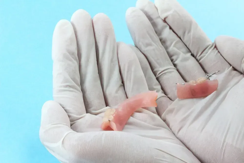 A Person Wearing Gloves is Holding a Denture in Their Hand — Twin Towns Denture Clinic In Forster, NSW
