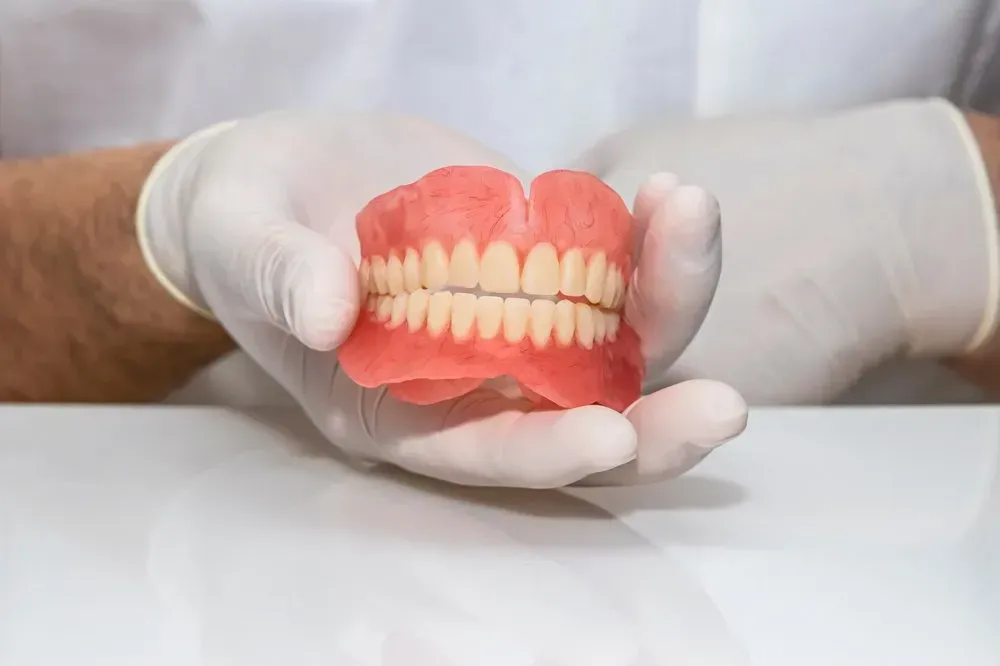 A Dentist is Holding a Full Denture in His Hands — Twin Towns Denture Clinic In Forster, NSW
