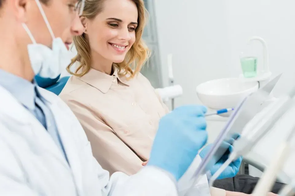 A Woman is Sitting in a Dental Chair While a Dentist Looks at a Tablet — Twin Towns Denture Clinic In Forster, NSW