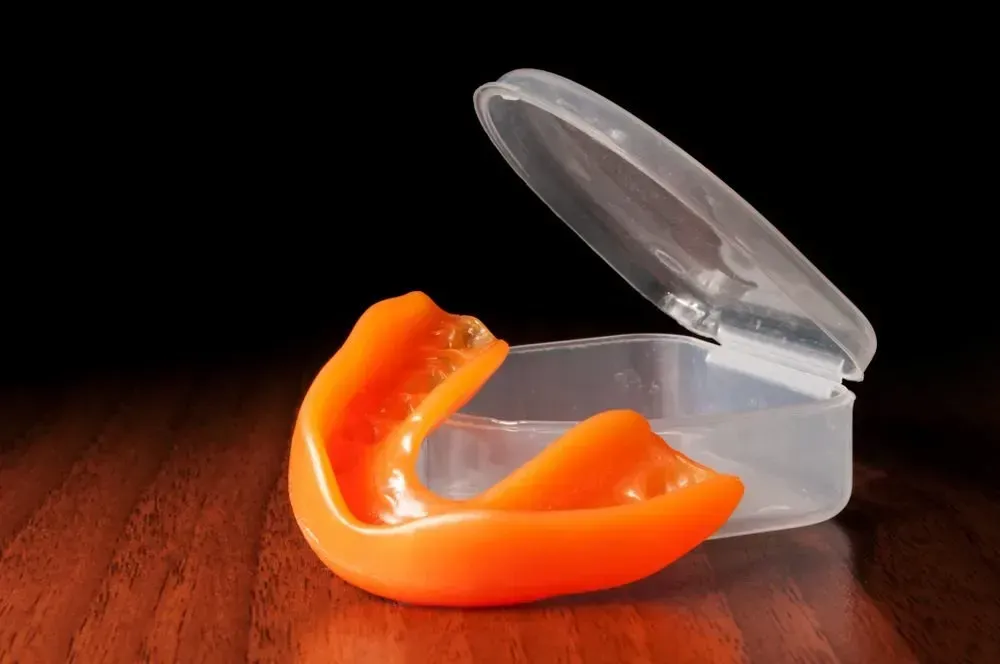 An Orange Mouth Guard is Sitting in a Plastic Case on a Wooden Table — Twin Towns Denture Clinic In Hawks Nest, NSW