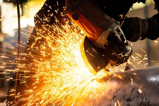 A person uses an angle grinder, creating sparks while working on metal in a workshop.