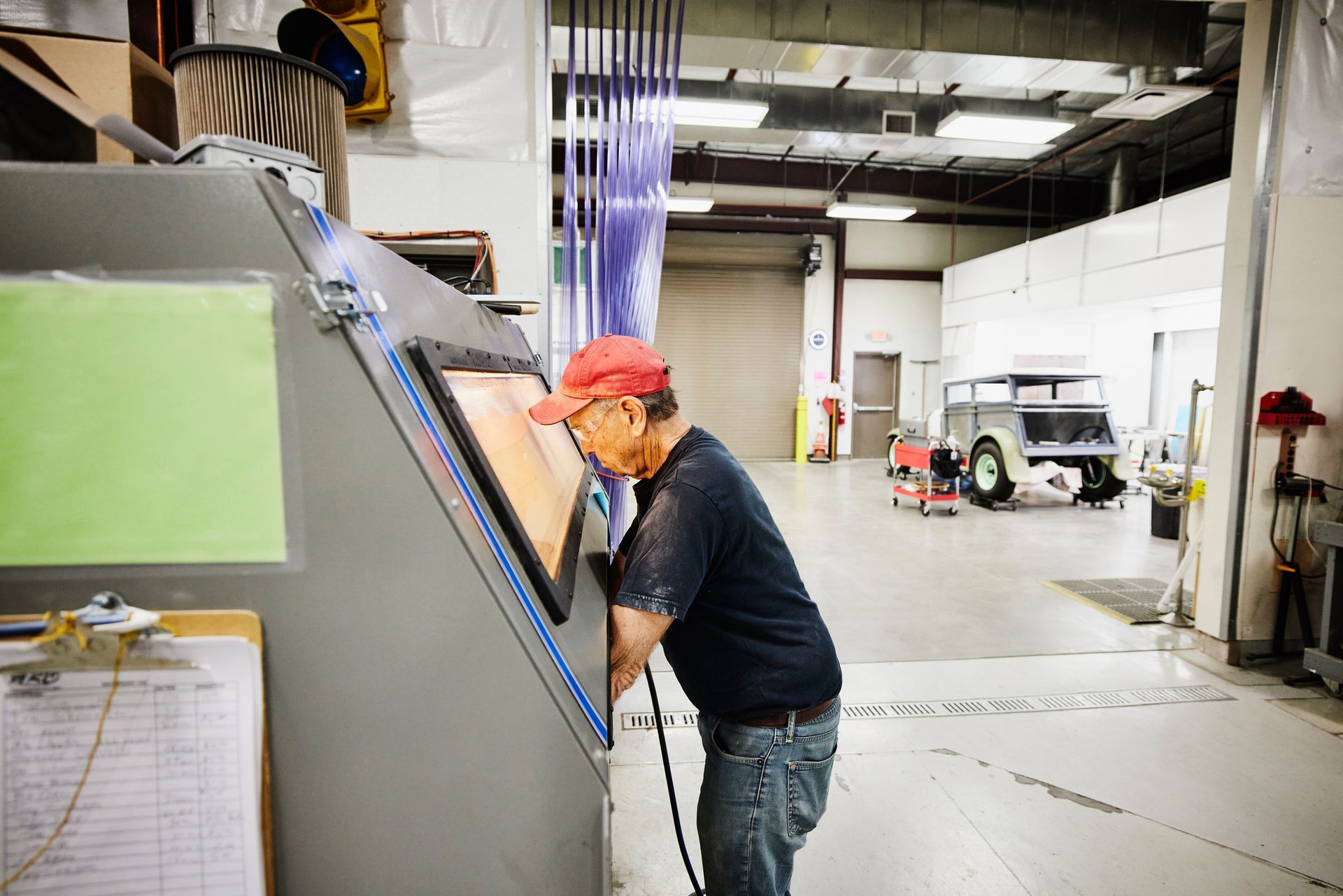 Man in a red cap works at a sandblasting machine in a workshop.