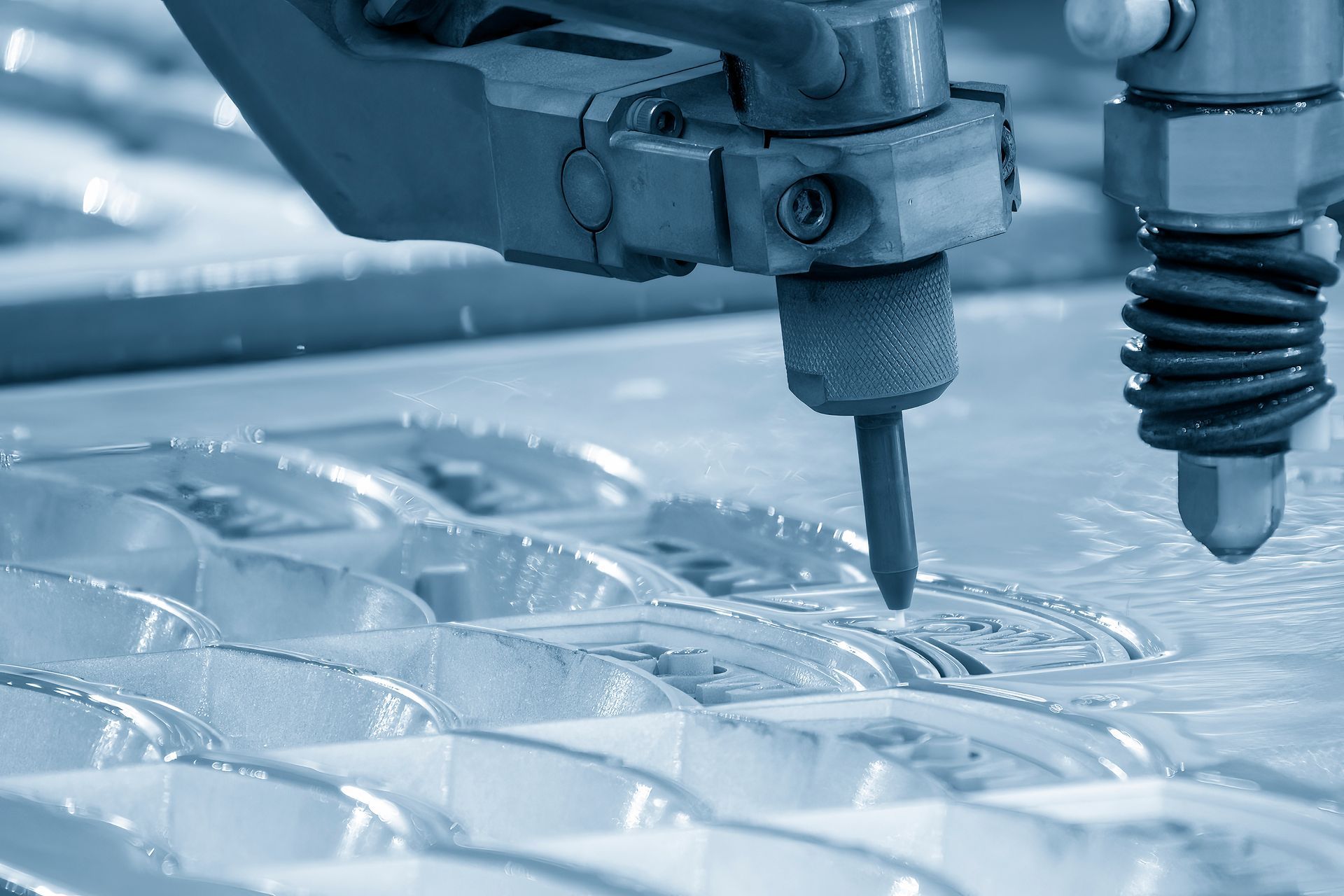 Waterjet cutter cutting a patterned design in a sheet of material. Blue-toned with water spraying.