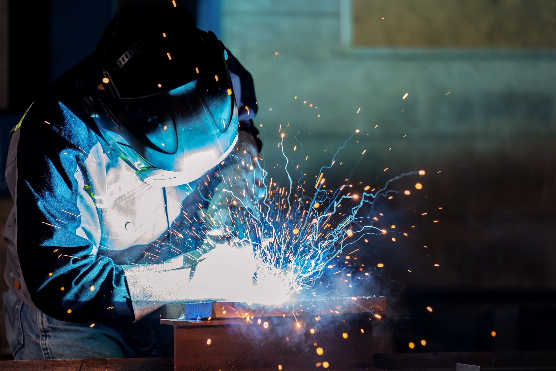 Welder wearing protective gear, working with sparks and bright light.