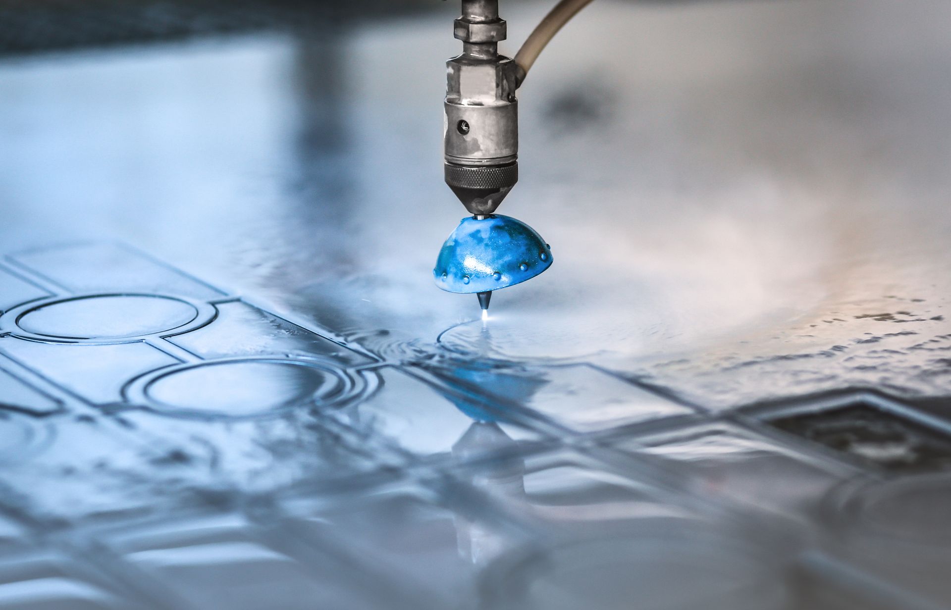 Water jet cutting a blue-tinted material, creating intricate designs; close-up view.