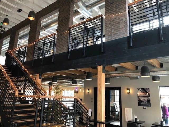 Two-story interior with staircase, brick walls, a balcony, and black industrial lighting.
