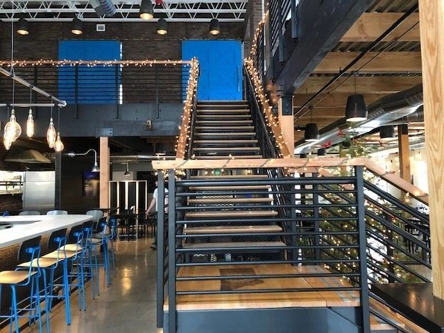 Interior with staircase, bar seating, and open space; black and wood tones. Blue accents, string lights.