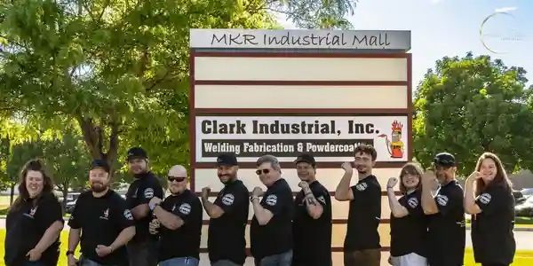 Group of people flexing their arms in front of a sign for Clark Industrial, Inc. and MKR Industrial Mall.