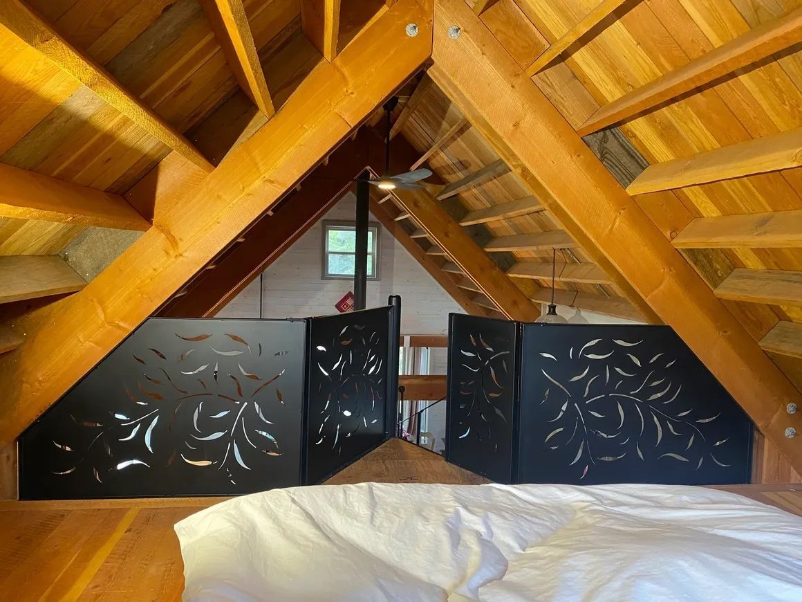 Loft bedroom with black decorative railing and wooden beams. White bedding.