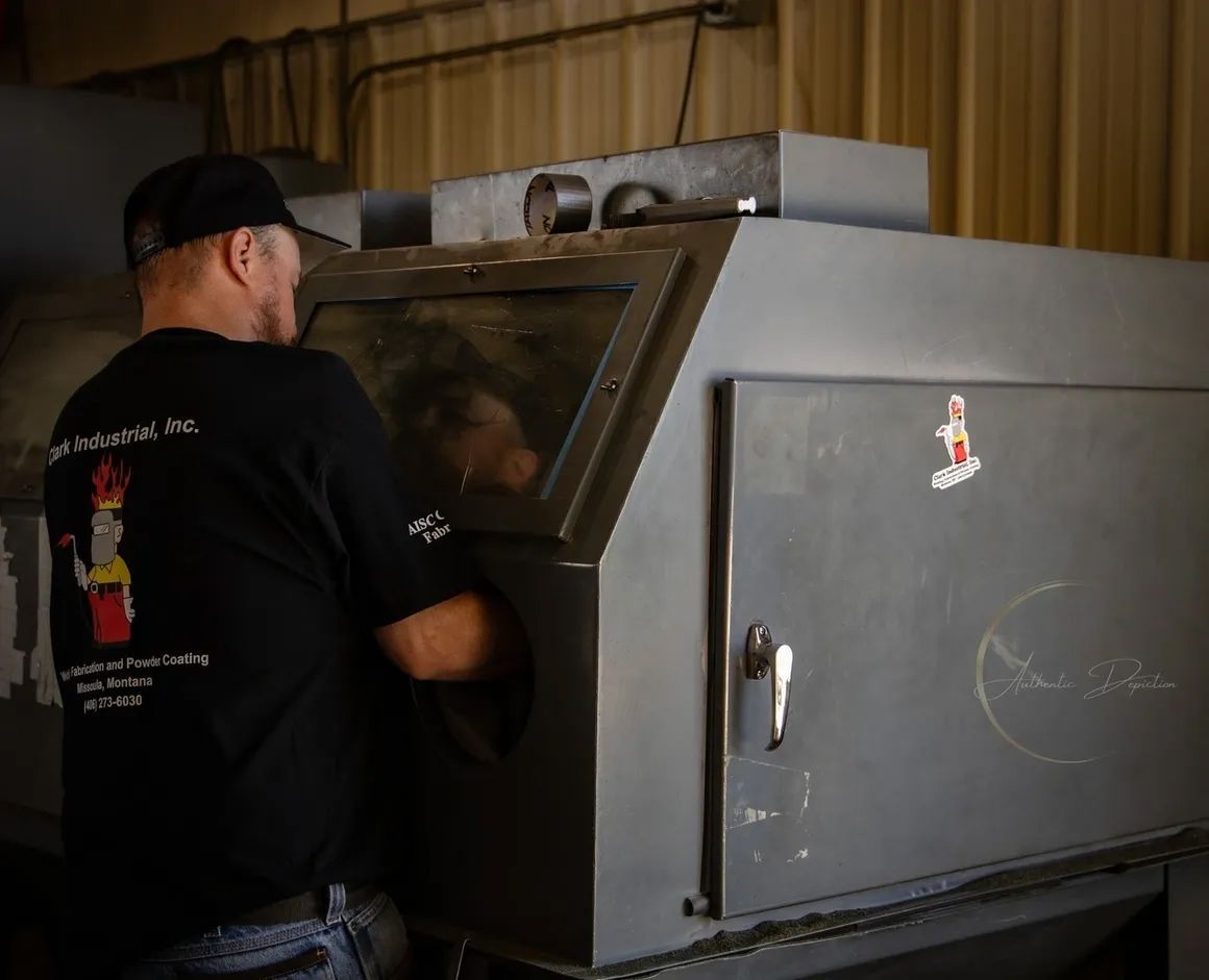 Man operating a sandblasting cabinet in a workshop. He's wearing a black shirt, and the machine is grey.