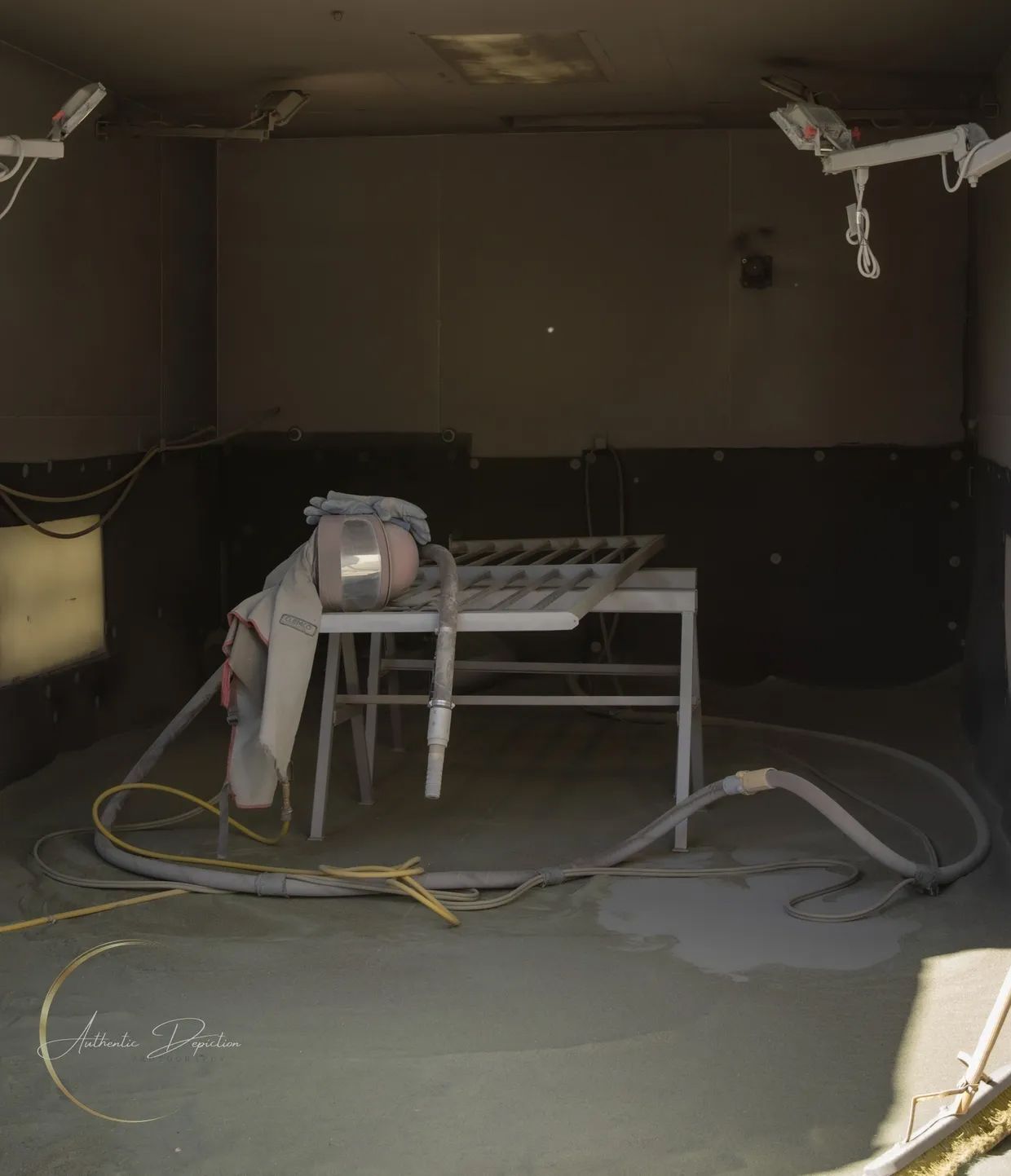 Interior view of a room coated in grey dust, with a table, hoses, and lights mounted on the ceiling.