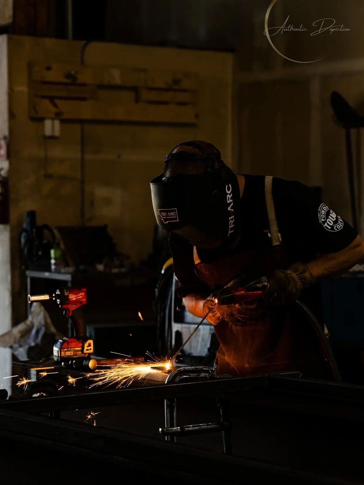 Welder wearing a mask, working with sparks in a dimly lit workshop.
