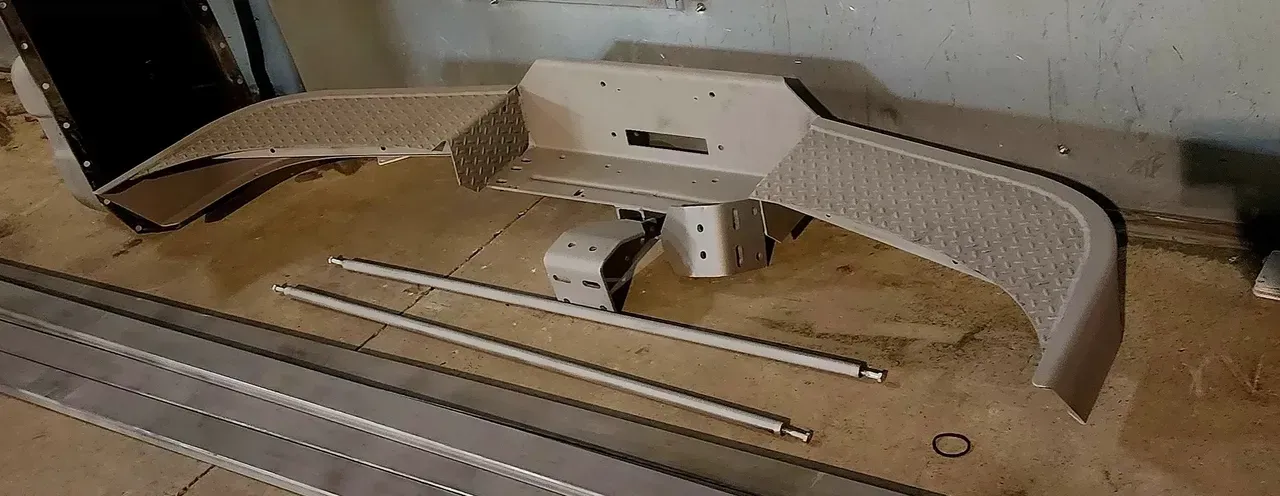 Metal vehicle components laid out on a wooden surface, ready for assembly.