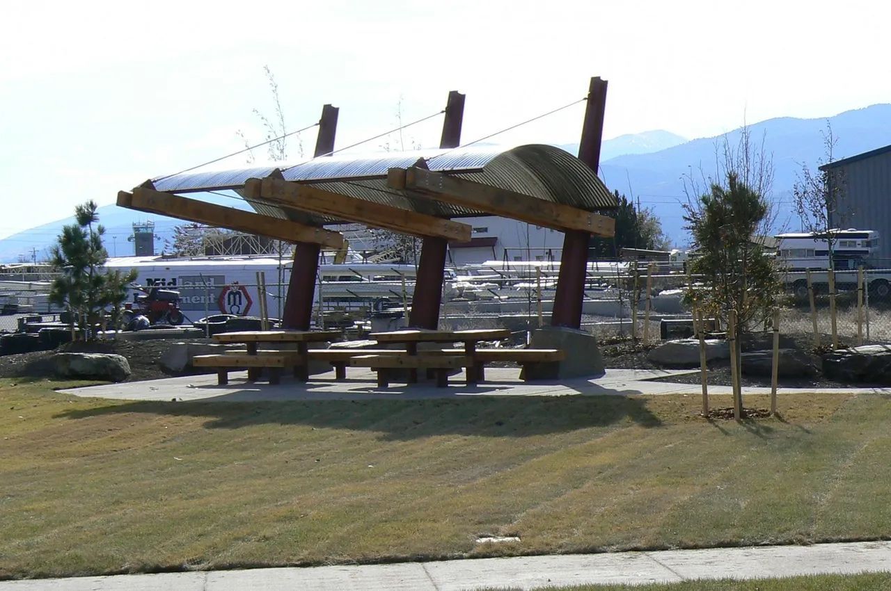 Picnic shelter in a park with wooden tables and a wavy roof; mountains in the background.