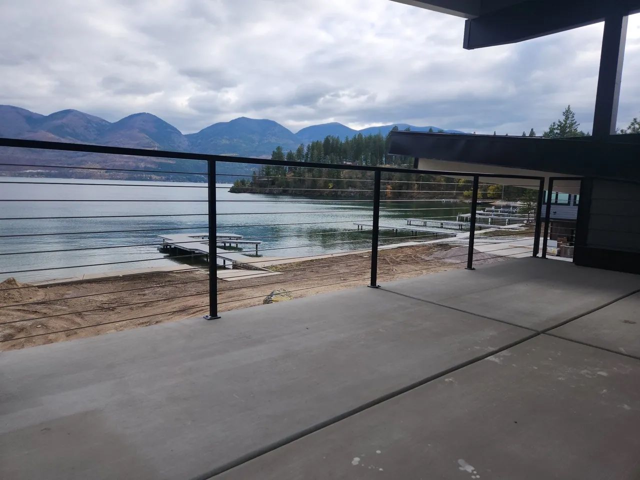 View from a concrete patio overlooking a lake and mountains, with a black railing.