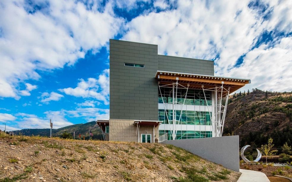 Modern building with gray and glass facade against a blue sky with clouds.