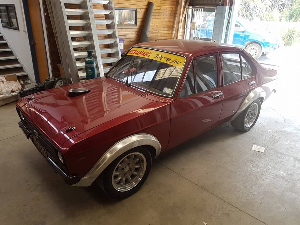 A red car with a yellow banner on the windshield is parked in a garage.