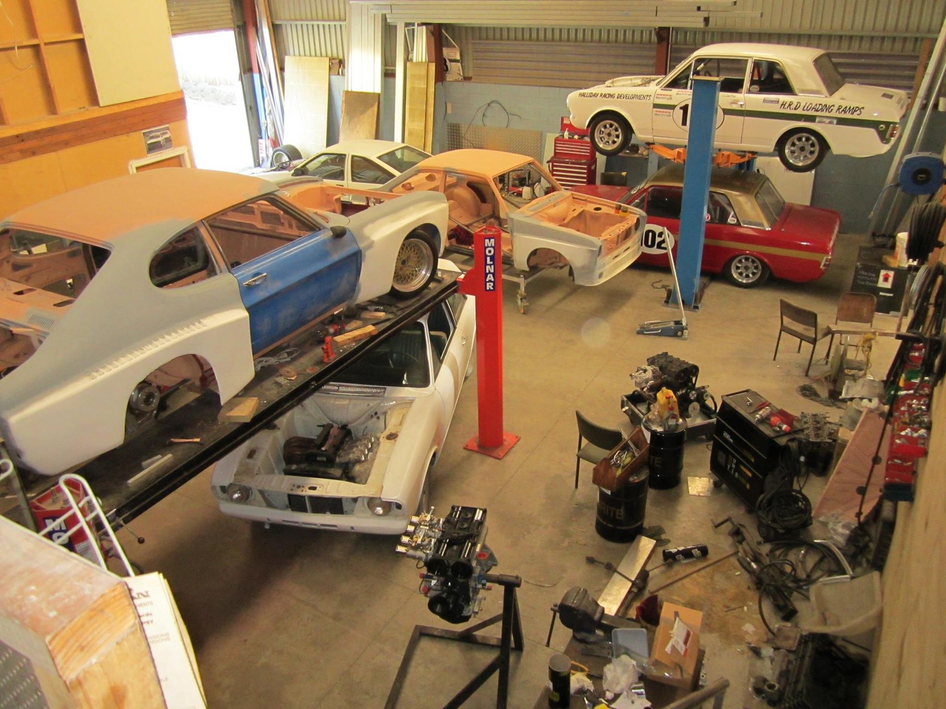 A lot of cars are sitting in a garage including a ford.