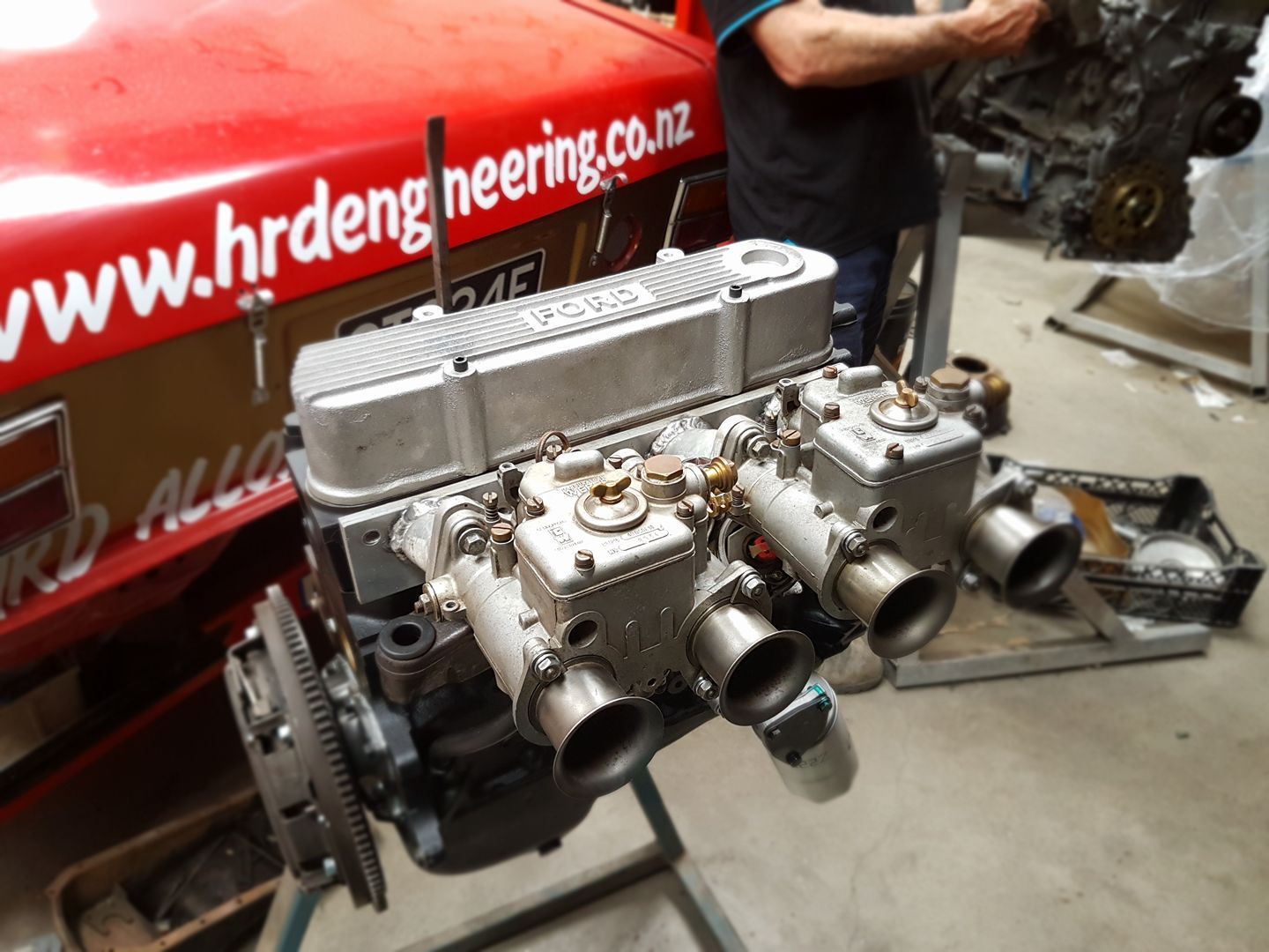 A man stands in front of a red car.