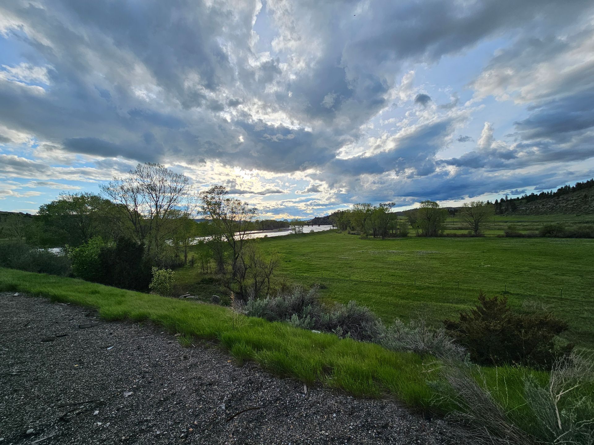 A cloudy sky over a grassy field with a river in the background.