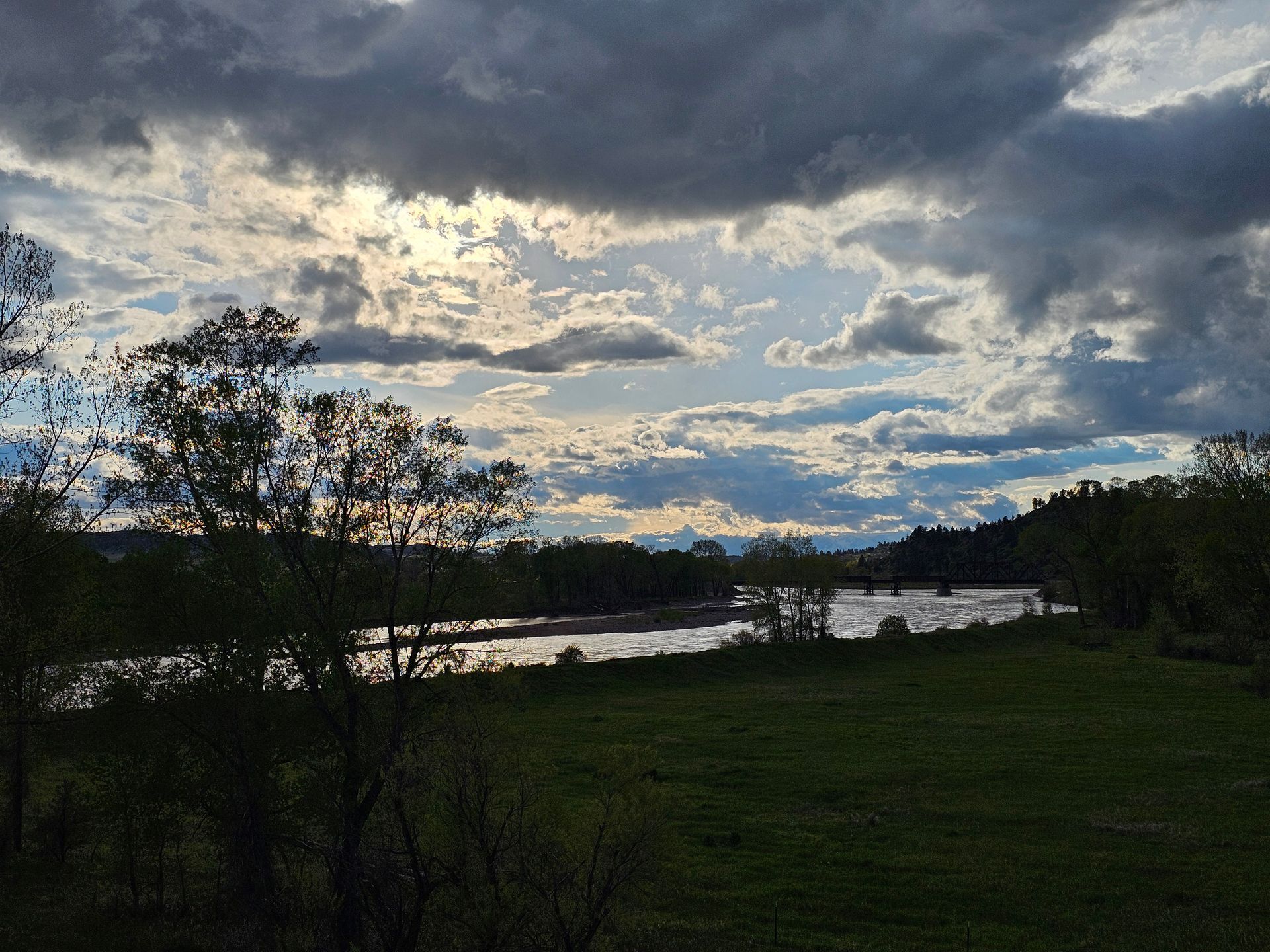 A cloudy sky over a lake with trees in the foreground