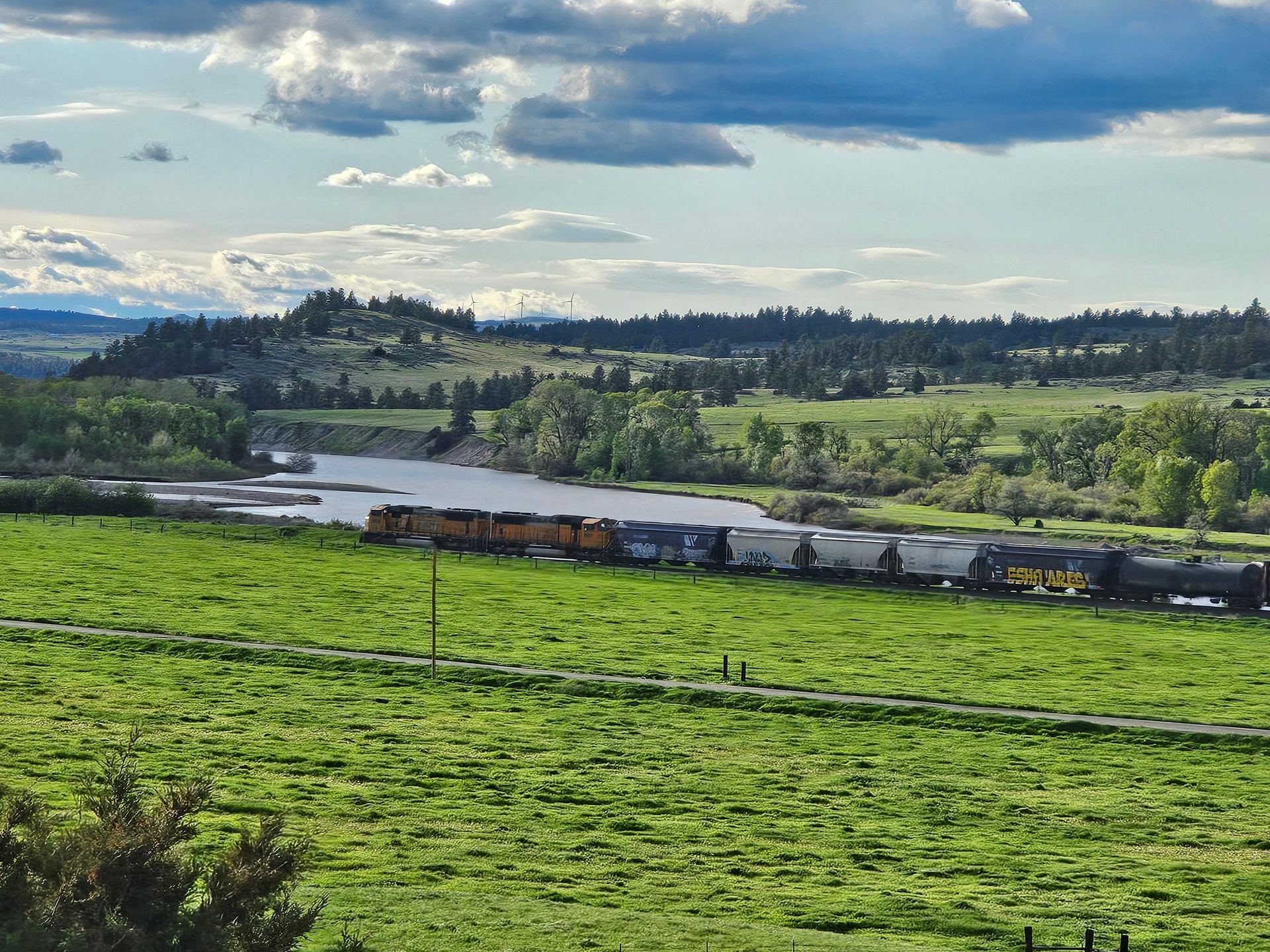 A train is going through a grassy field next to a river.