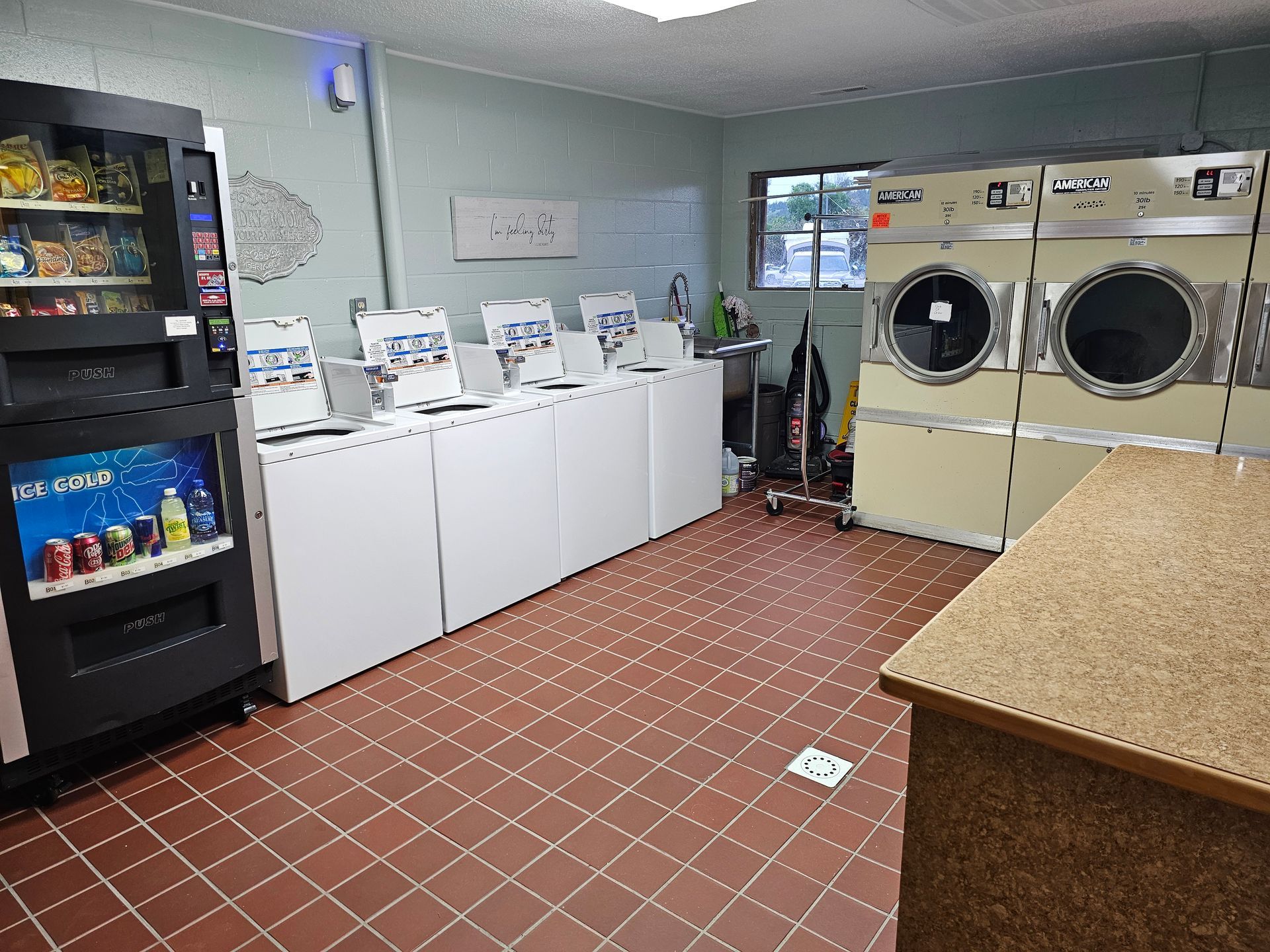Laundry room with washers, dryers, vending machine, and folding table. Red tile floor.