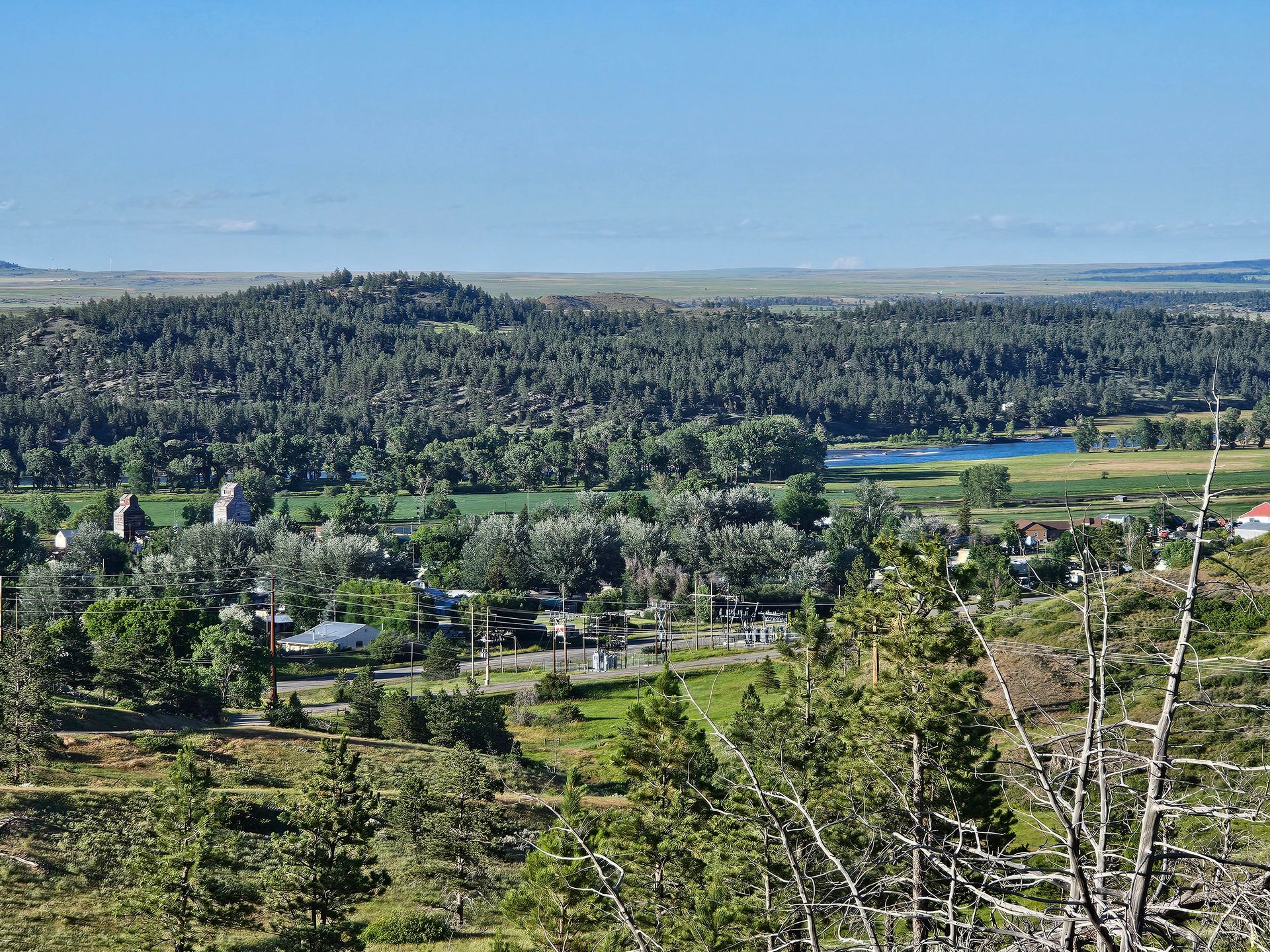Overlook of a small town with green fields and a dense forest, under a blue sky.