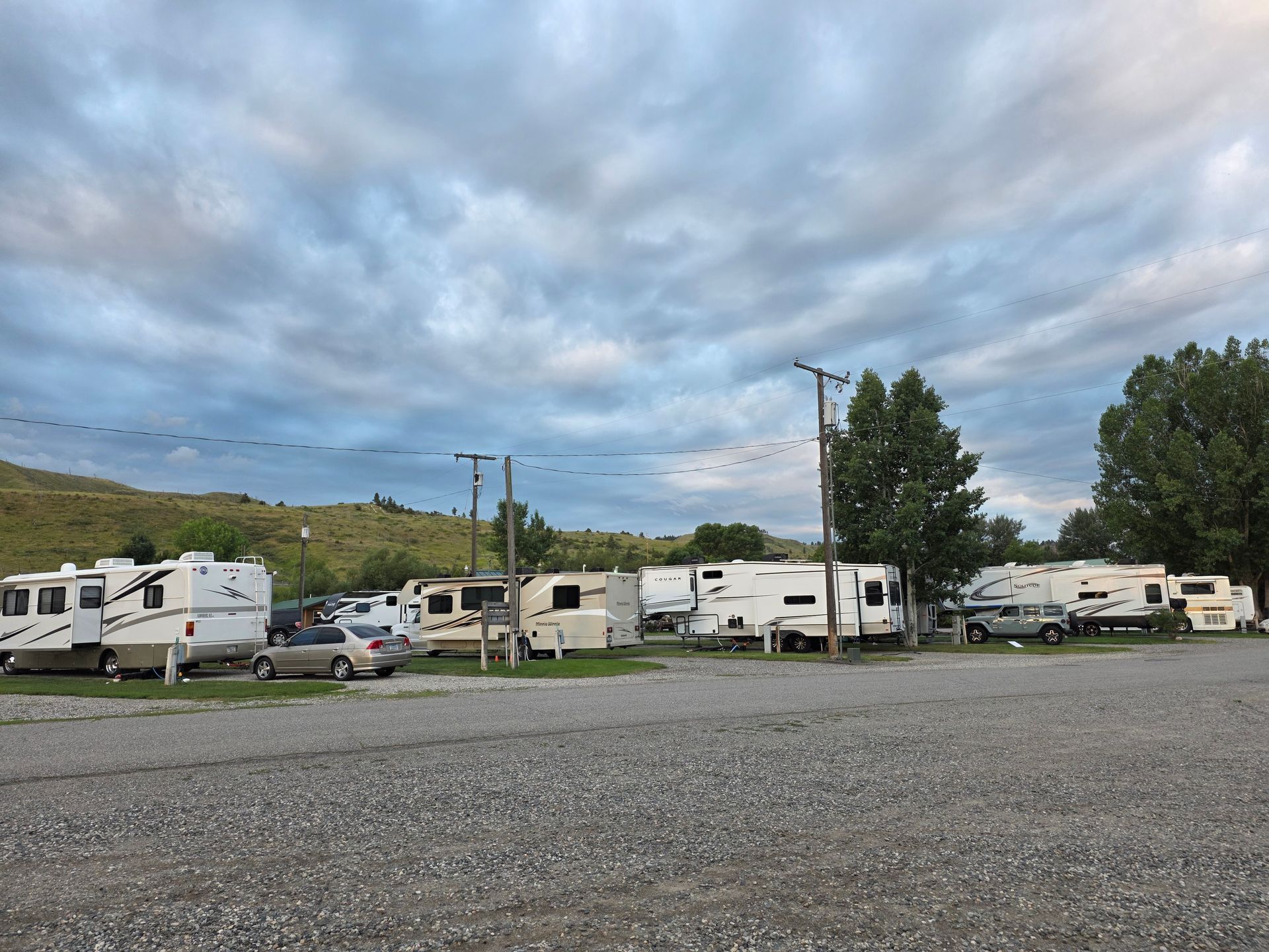 RV campground with gravel parking, parked RVs, and overcast sky.