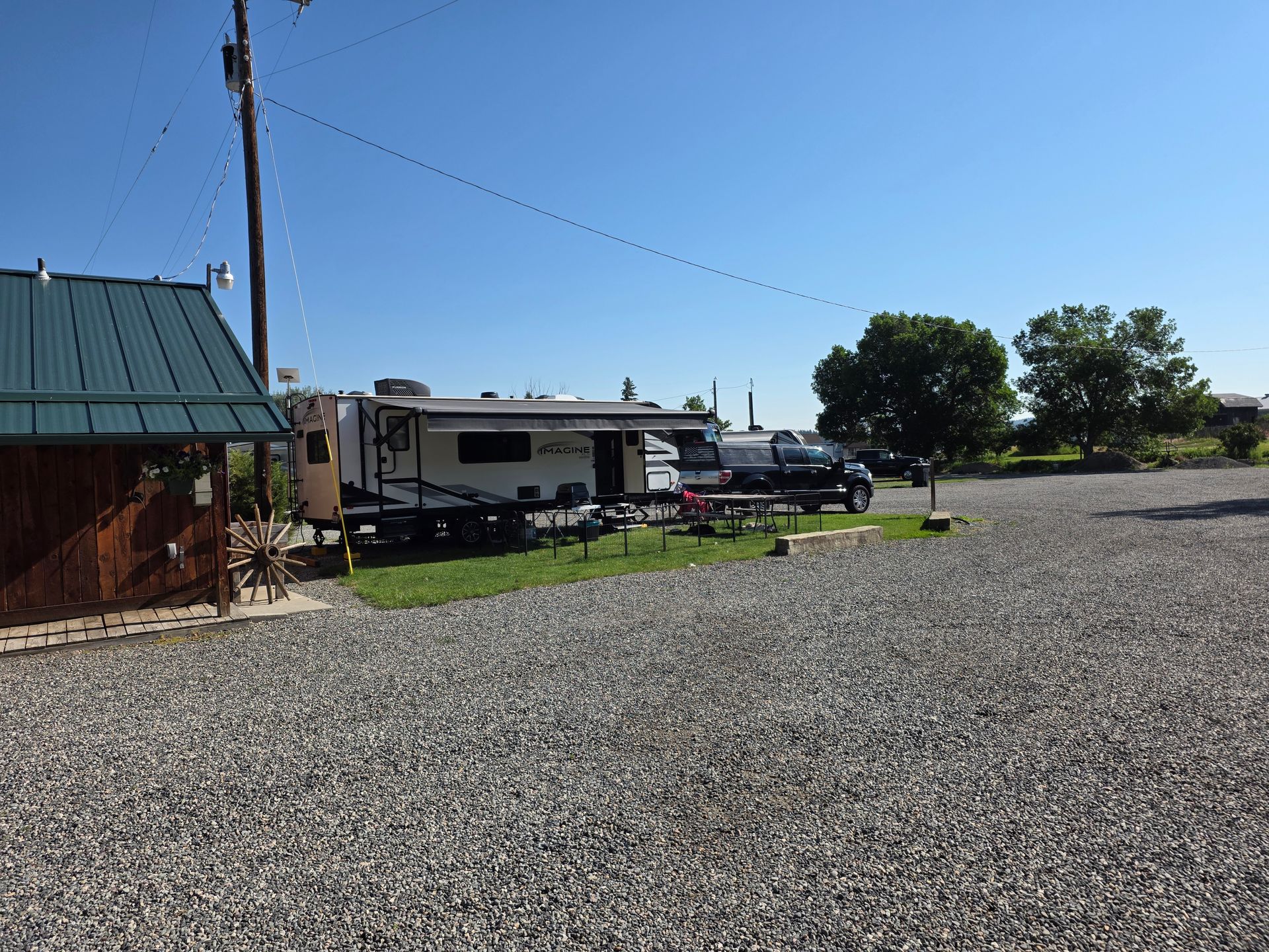 RV parked on gravel next to a small building with a green roof under a clear blue sky.